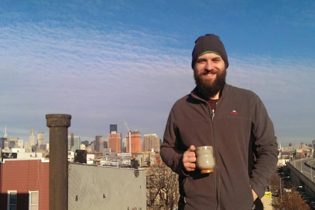 Jag på ett tak i New York, med en kaffemugg i handen och Manhattan i bakgruden och ett stort leende på läpparna.